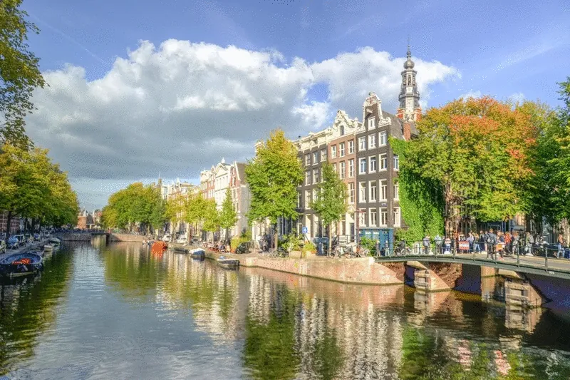 Canal houses and autumn trees along a canal in Amsterdam, with a church tower behind them